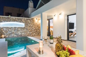 Un área de piscina al aire libre con un muro de piedra, un bar con una vela y un frutero.