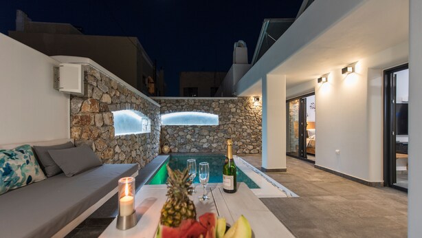 A modern outdoor seating area with a stone wall, a pool, and a table with fruits and a bottle.