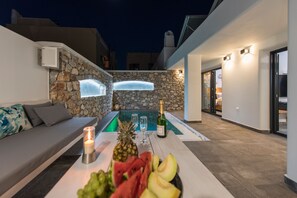 Un área de estar moderna al aire libre con pared de piedra, piscina y una mesa con frutas y una botella.