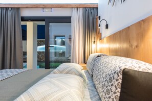 A modern hotel room with a large bed, a wooden headboard, and a glass door leading to a balcony.