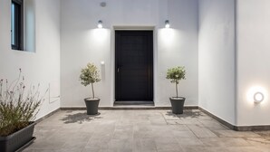 A modern entrance with a black door, two potted plants, and wall-mounted lights.