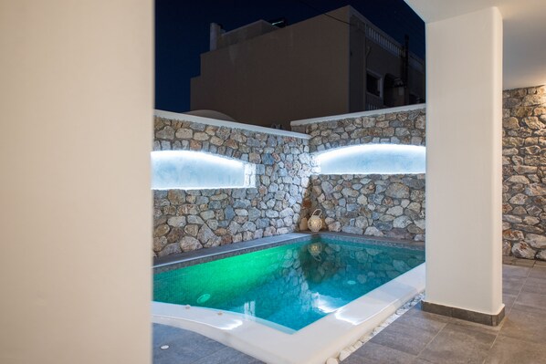 Una piscina con paredes y piso de piedra, rodeada por un edificio blanco.