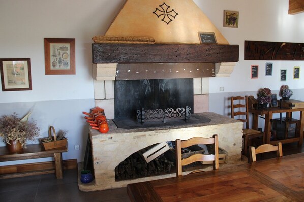 A rustic fireplace with a stone surround, a wooden bench, and a dining table with chairs.