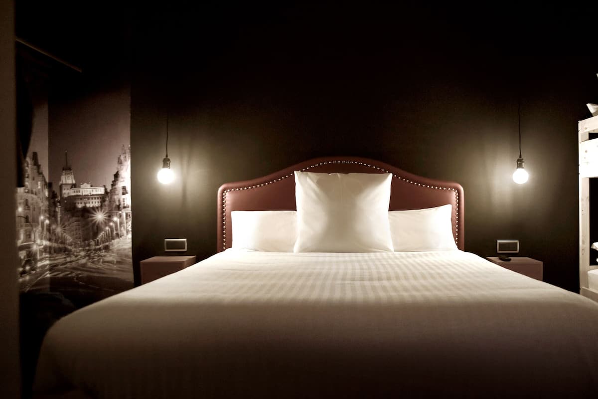 Un lit bien fait, avec une tête de lit, deux tables de chevet et un luminaire fixé au mur.