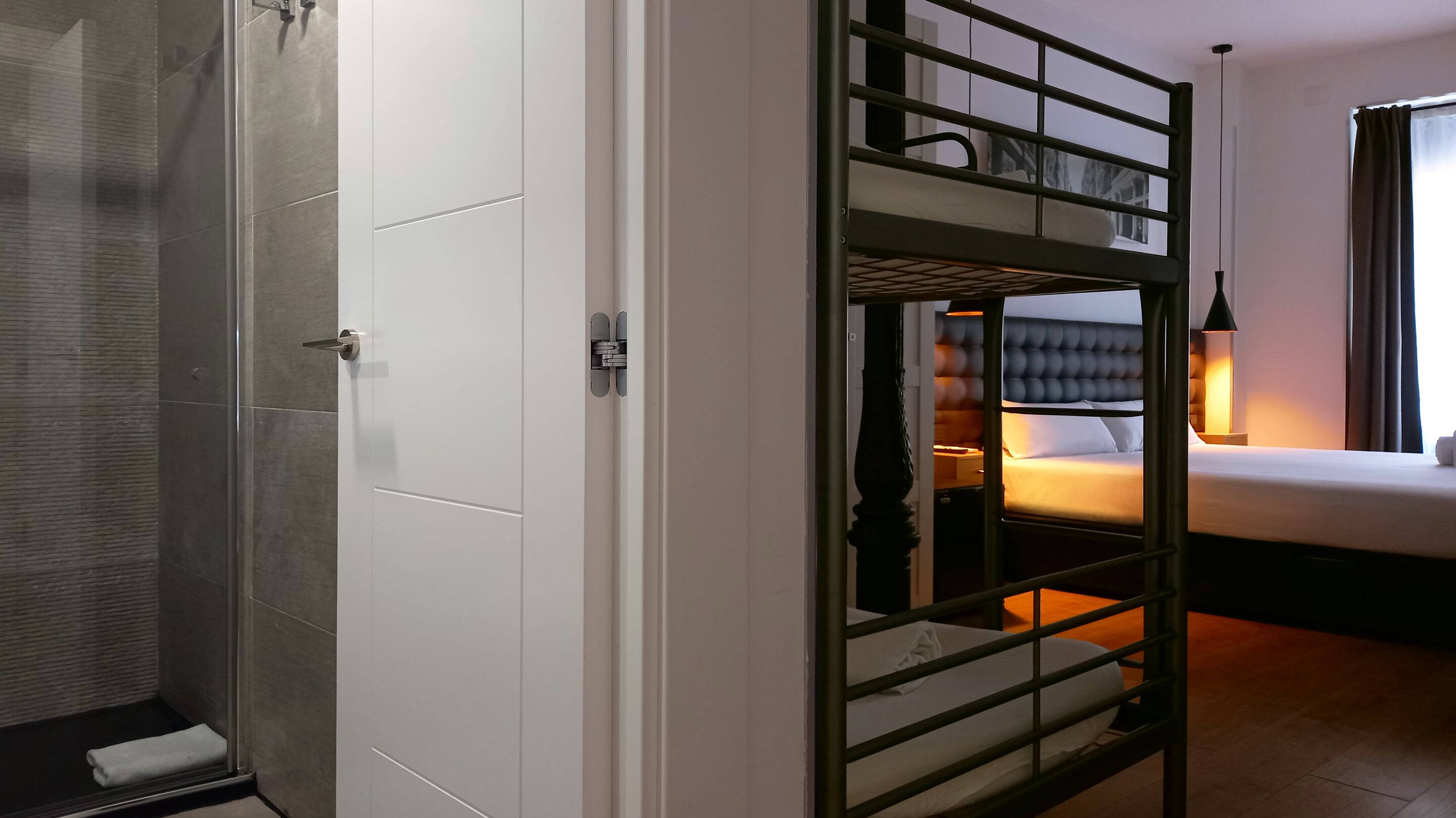 Habitación de hotel con ducha, cama con cabecero y mesita de noche con lámpara.