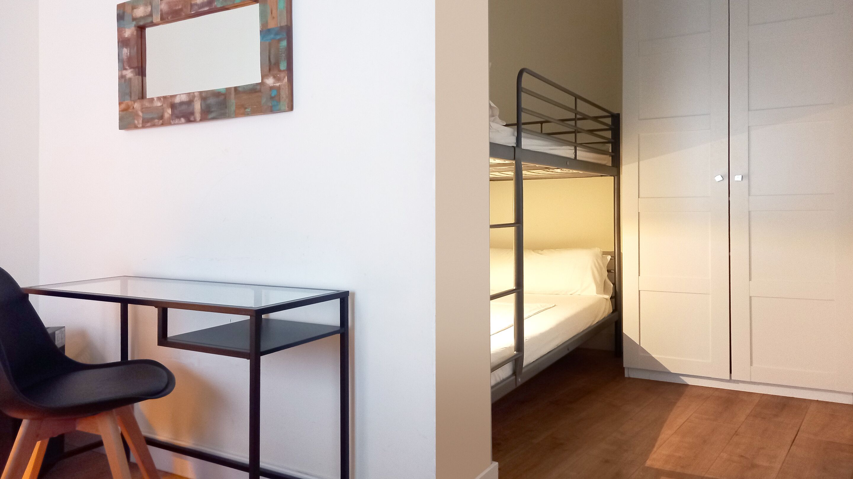 A room with a bunk bed, a glass desk, a chair, and a wardrobe.