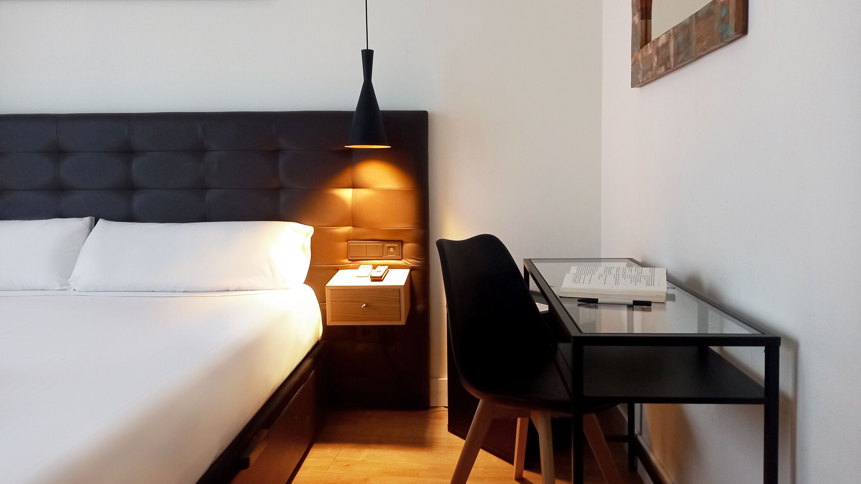 A hotel room with a bed, bedside table, lamp, chair, and a desk with a chair.