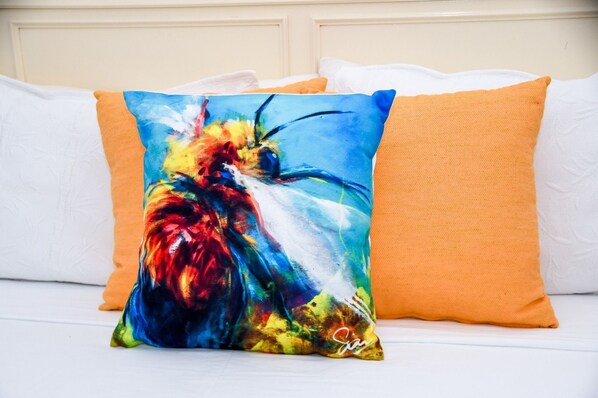Una cama con almohadas blancas y anaranjadas, una de ellas con un diseño abstracto y colorido.
