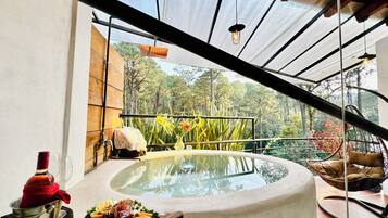 A glass-top table with a variety of food items and a bottle, set against a backdrop of a balcony with a view of trees and a hanging light fixture.