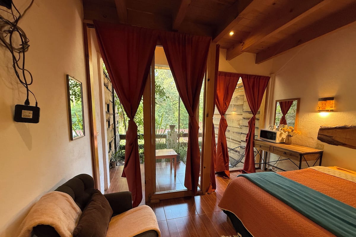 Una habitación con cama, escritorio, silla y ventana con cortinas.