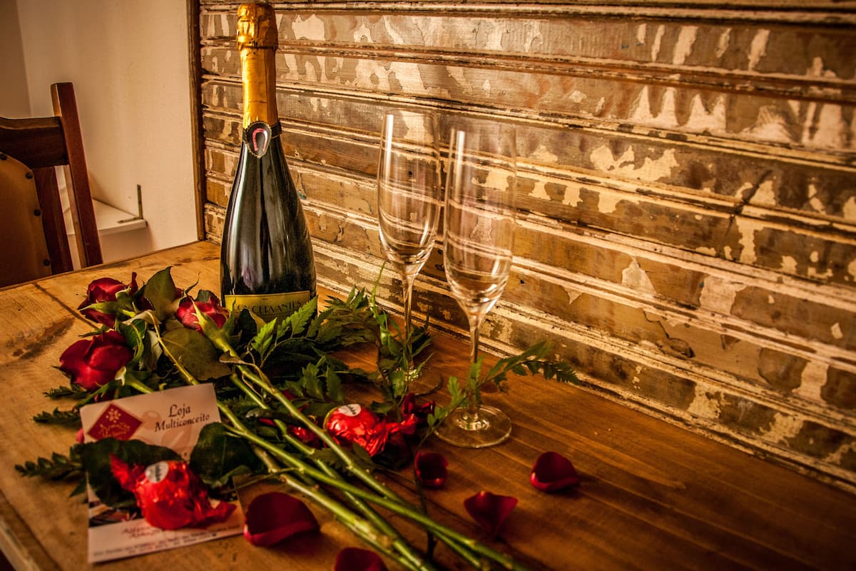 Una mesa de madera con una botella de champán, dos copas de vino vacías y pétalos de rosa esparcidos.