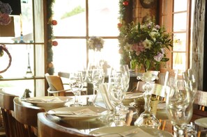 Una mesa de comedor dispuesta con varios vasos de vino, platos y cubiertos, con un centro de mesa floral y vistas a la Torre Eiffel a través de grandes ventanales.