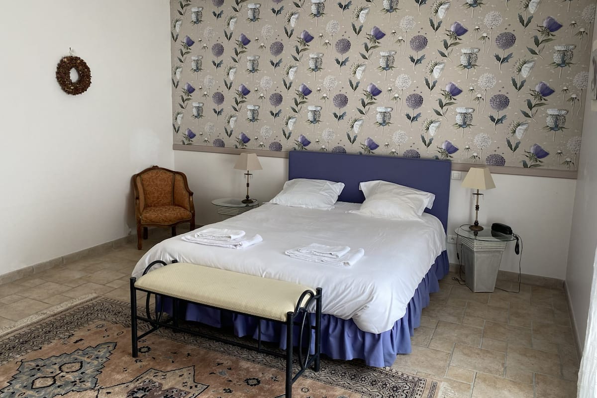 A neatly arranged bedroom with a bed, two bedside tables, a chair, and a patterned wallpaper.