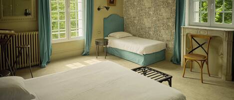 Un dormitorio con cama, una silla, un radiador y una ventana con cortinas.