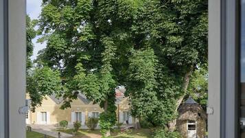 A view through a doorway of a courtyard with a large tree, a stone structure, and a building with a sloped roof.