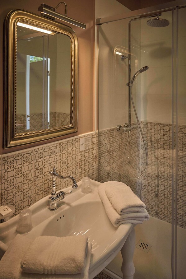 Un baño con lavamanos blanco, espejo y cabina de ducha.
