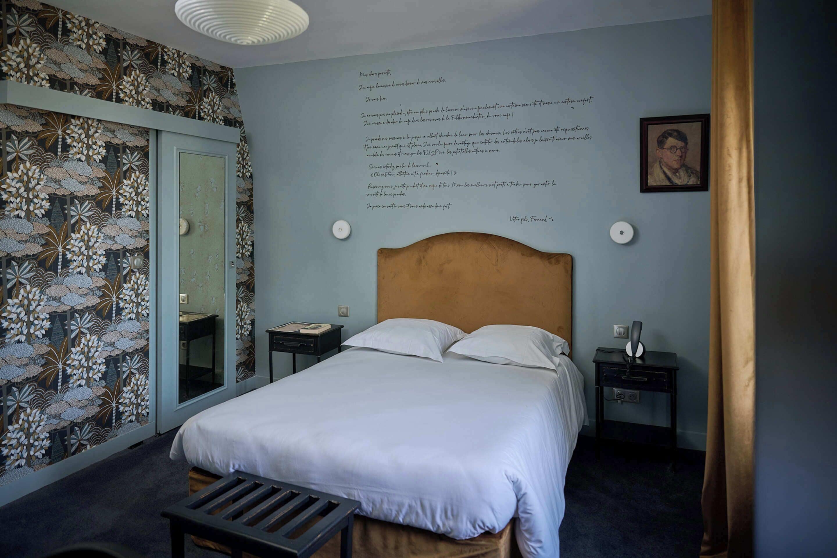 Une chambre à coucher avec un lit, des tables de chevet, un miroir et un mur orné de texte.