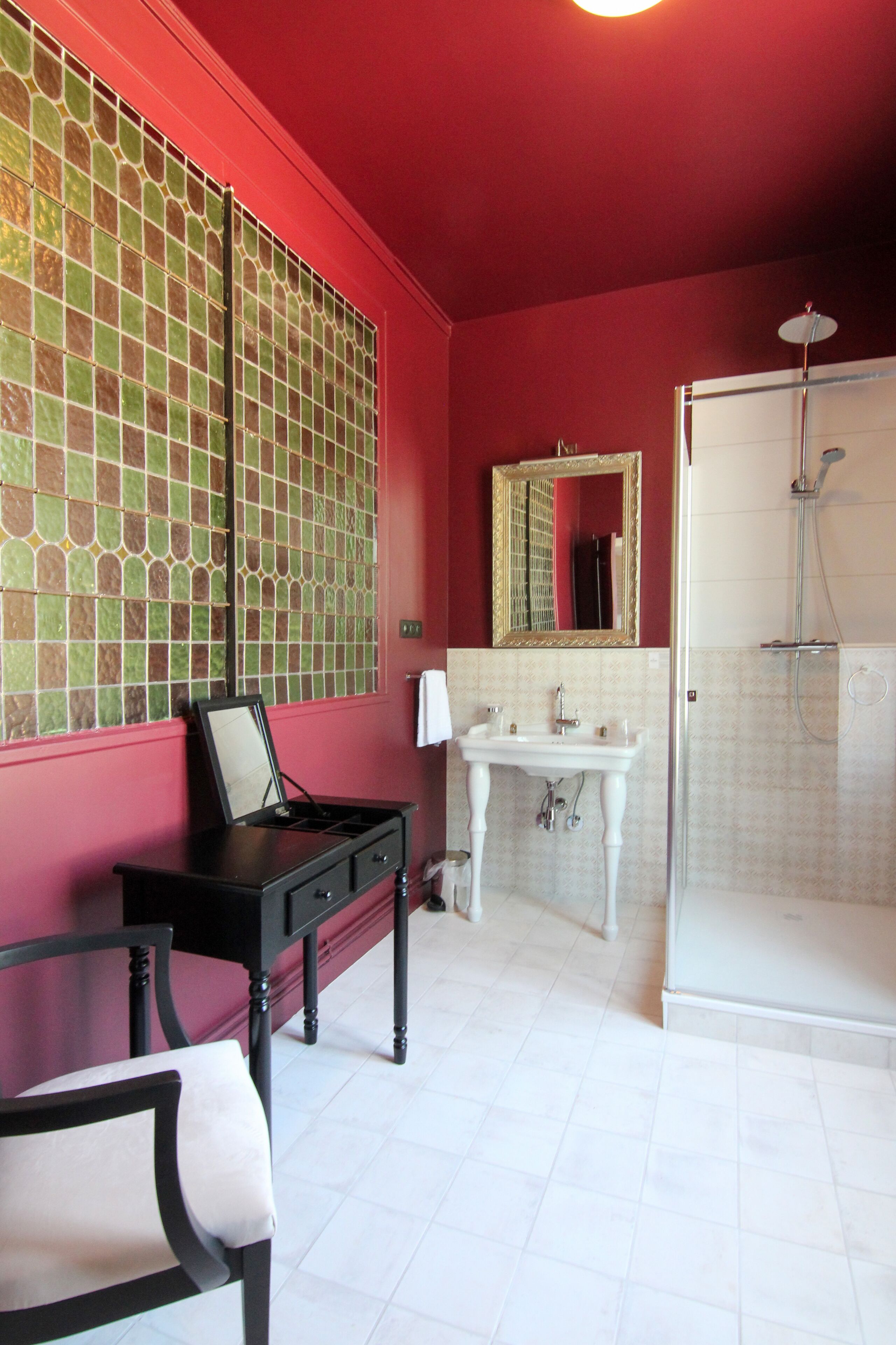 A bathroom with a red wall, a tiled shower area, a white sink, and a mirror.