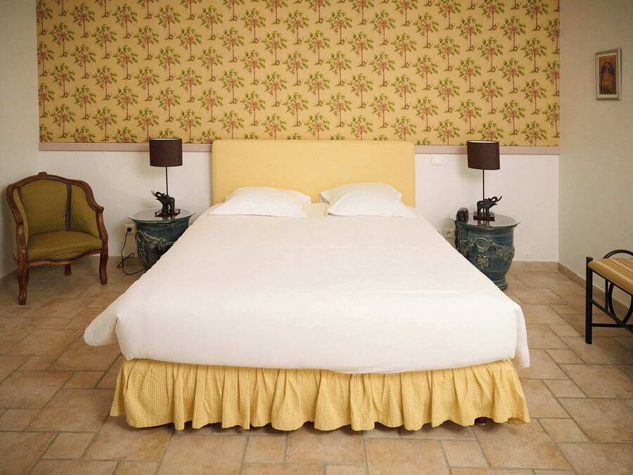 Un lit bien fait, avec une couvre-lit jaune, deux tables de chevet avec des lampes, une chaise et un banc.