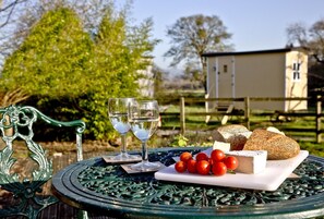 A table with a white plate of cheese, tomatoes, and bread, two glasses of water, and a green metal chair. - Middlewick Holiday Cottages (Glastonbury)