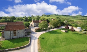Un village rural avec des bâtiments en pierre, une route sinueuse et des champs verdoyants.