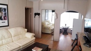 Una sala de estar con un sofá blanco, una mesa de centro oscura y un mueble de televisión con televisor de pantalla plana y control remoto.