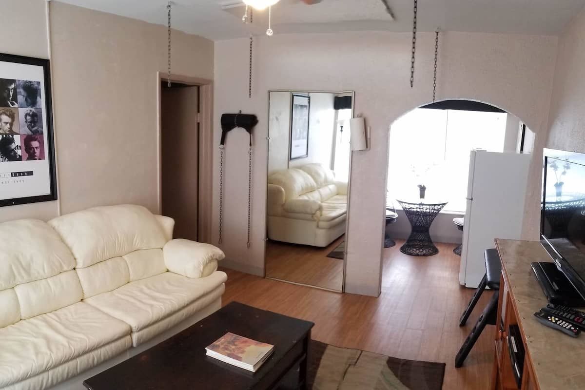 Un salon avec un canapé blanc, une table basse foncée et un meuble TV sur lequel est posée une télévision à écran plat ainsi qu’une télécommande.