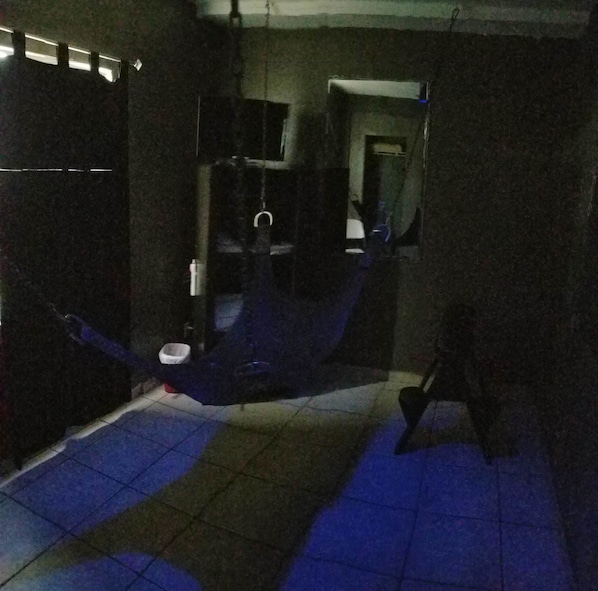 Una habitación tenuemente iluminada con una cama, una mesita pequeña y una silla. Se ve una ventana con vistas al exterior.
