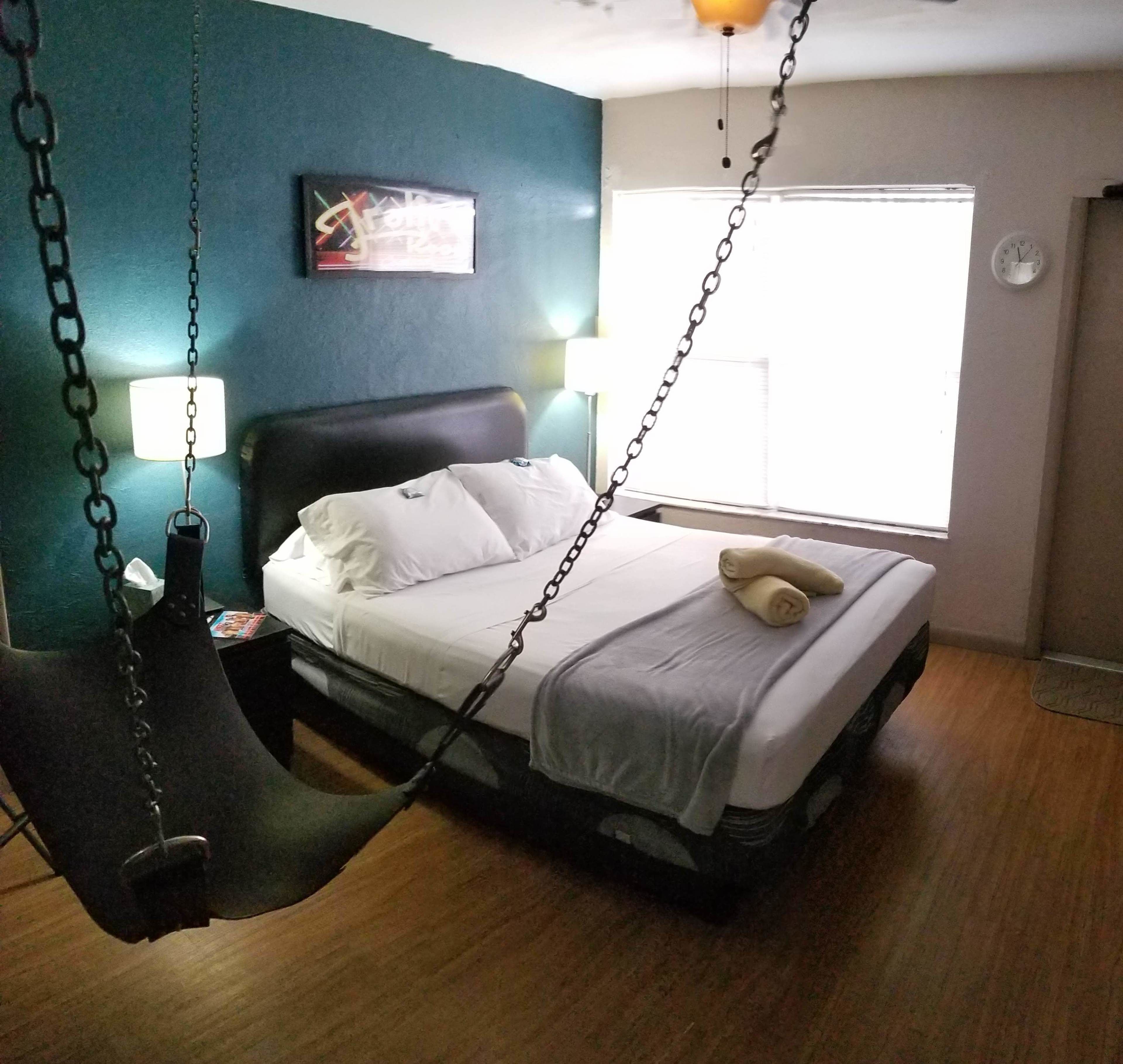 Quarto com cama, cadeira suspensa, mesa de cabeceira, luminária e janela com persianas.