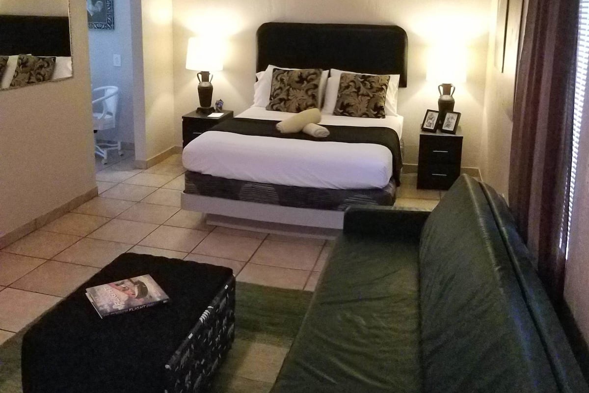 Une chambre d’hôtel avec un lit, des tables de chevet, un canapé, une petite table avec un magazine et une valise.