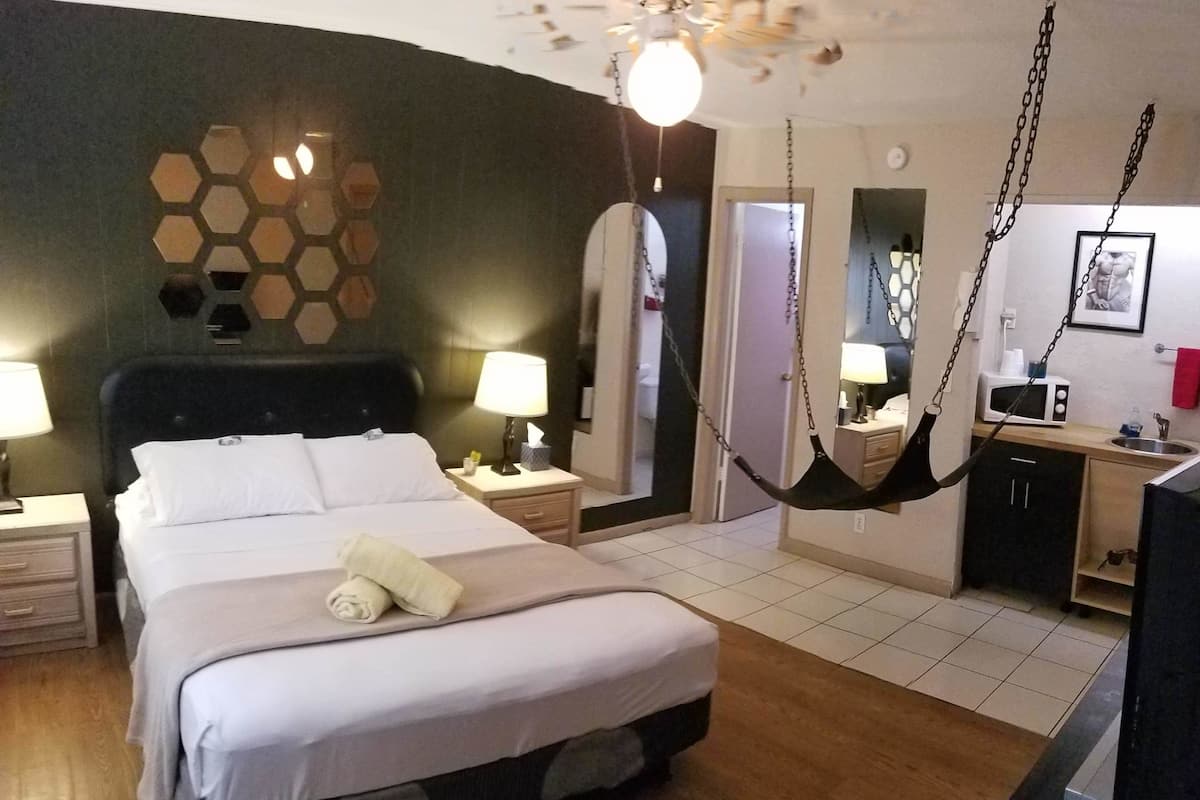 Une chambre d’hôtel avec un grand lit, des lampes de chevet, un fauteuil suspendu, une petite kitchenette et un miroir au mur.