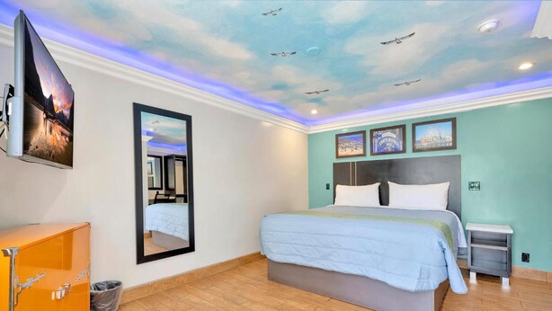 A hotel room with a large bed, a nightstand, a mirror, and a ceiling with a bird mural. - Mid City inn (Los Angeles)