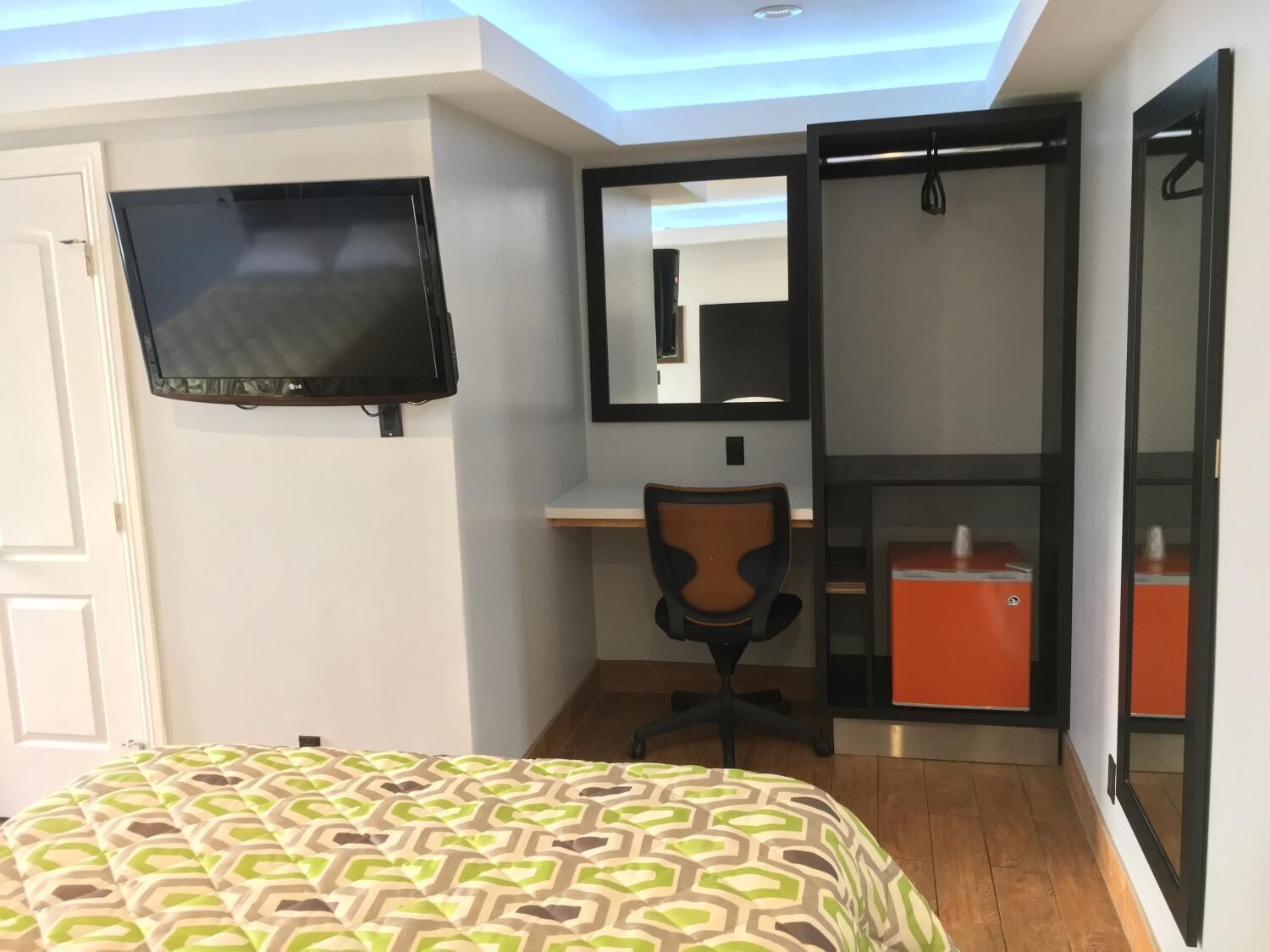 A bedroom with a bed, a desk, a chair, a TV, and a wardrobe.