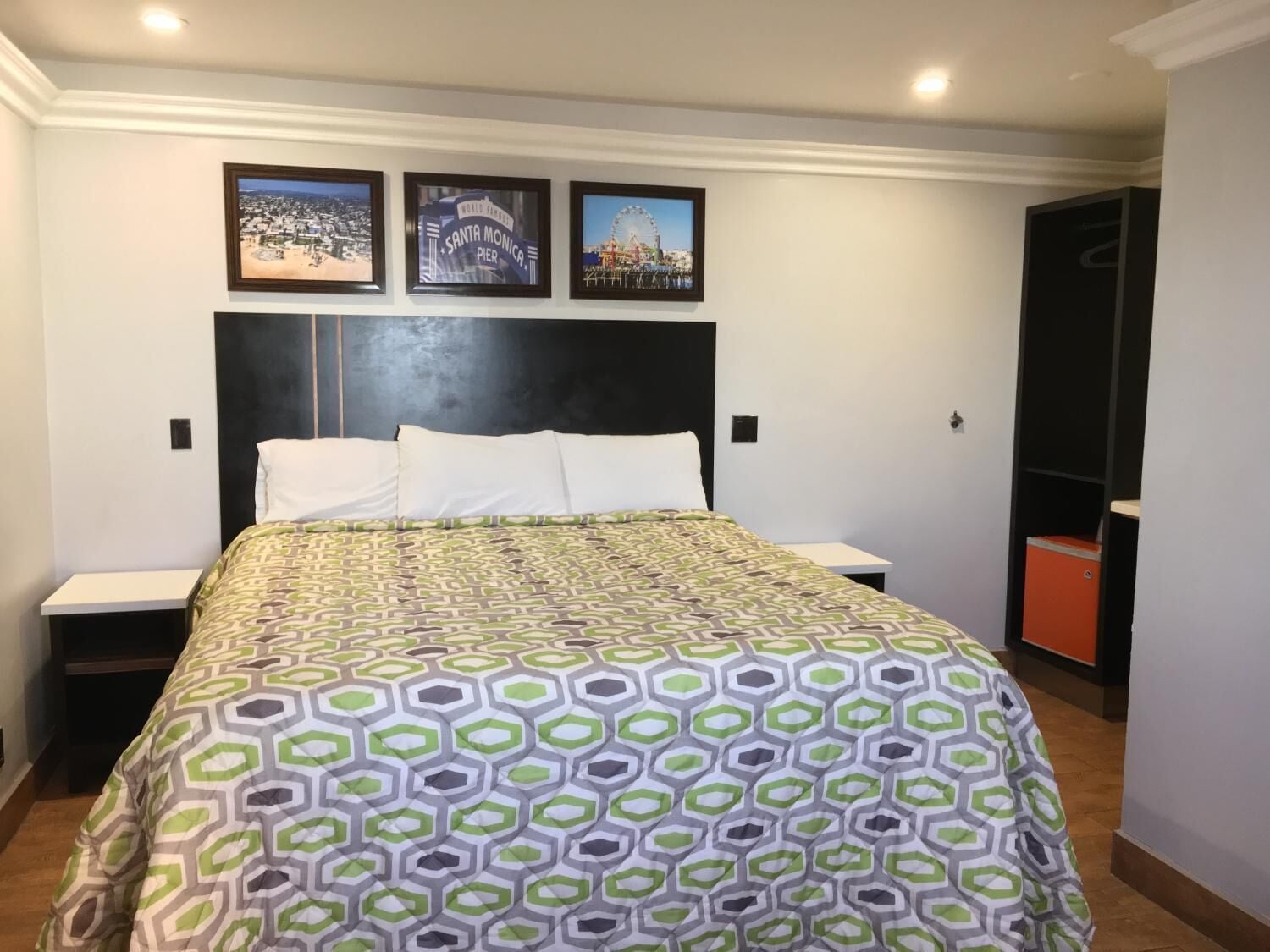 A hotel room with a bed, a nightstand, a wardrobe, and three framed pictures on the wall.