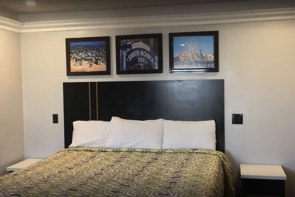 Une chambre d’hôtel avec un grand lit, une tête de lit noire et trois tableaux encadrés accrochés au mur.