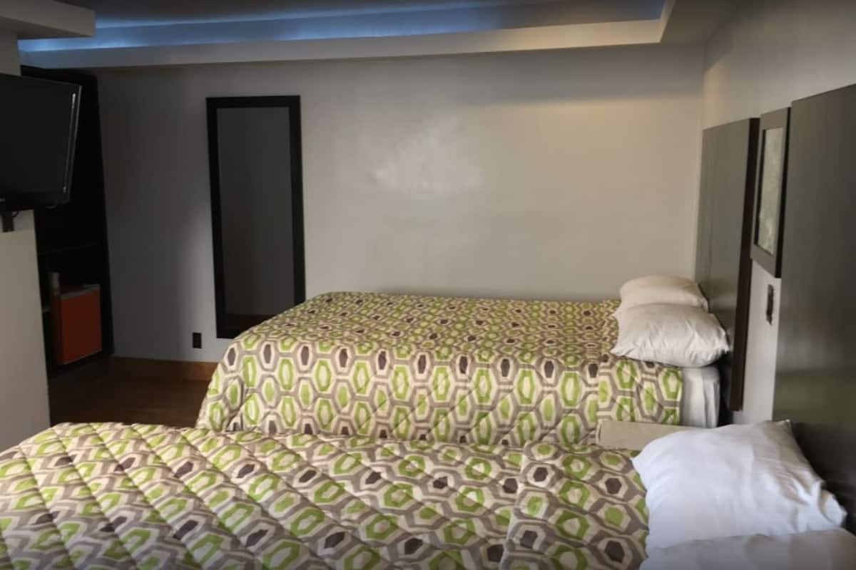 Une chambre avec deux lits, un téléviseur fixé au mur et une porte visible au fond.