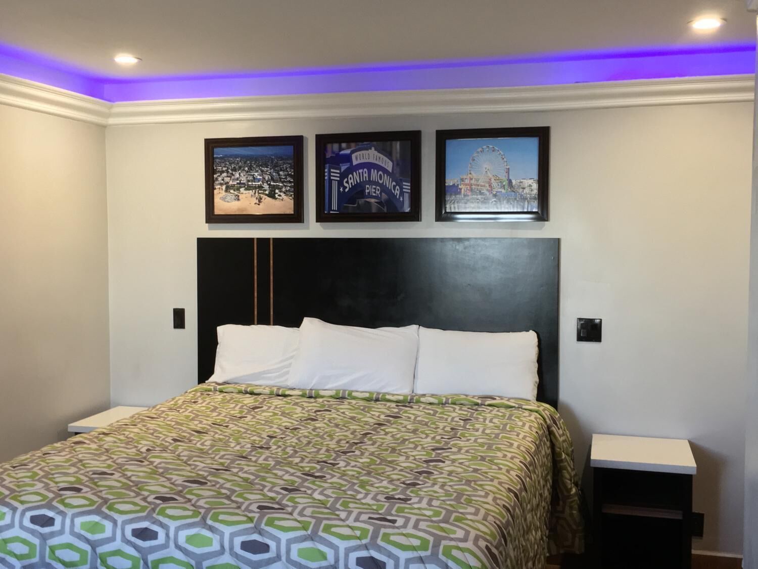 Een slaapkamer met een groot bed, een zwart hoofdeinde en drie ingelijste foto’s aan de muur.