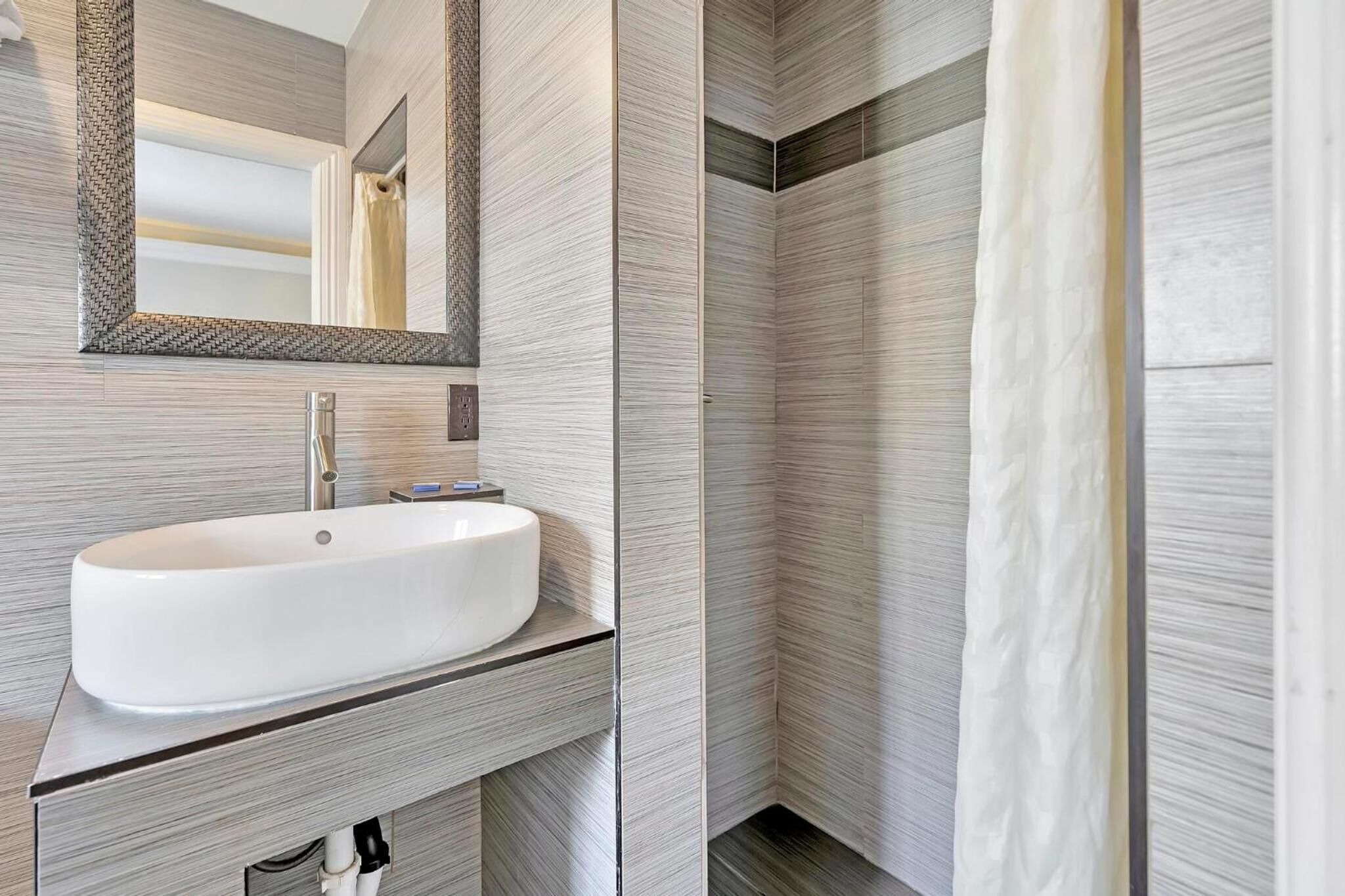Een moderne badkamer met een grote witte wastafel, een spiegel en een douchegordijn.
