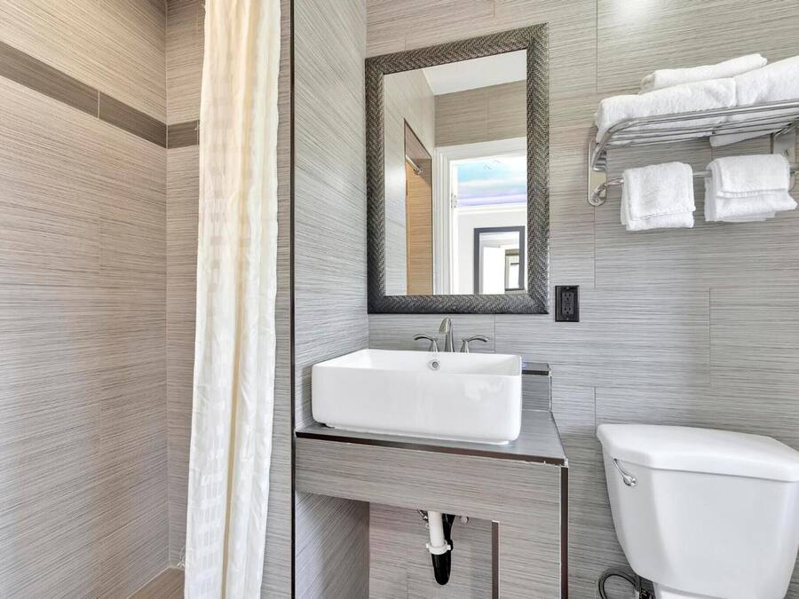 A modern bathroom with a large mirror, a white sink, and a toilet.