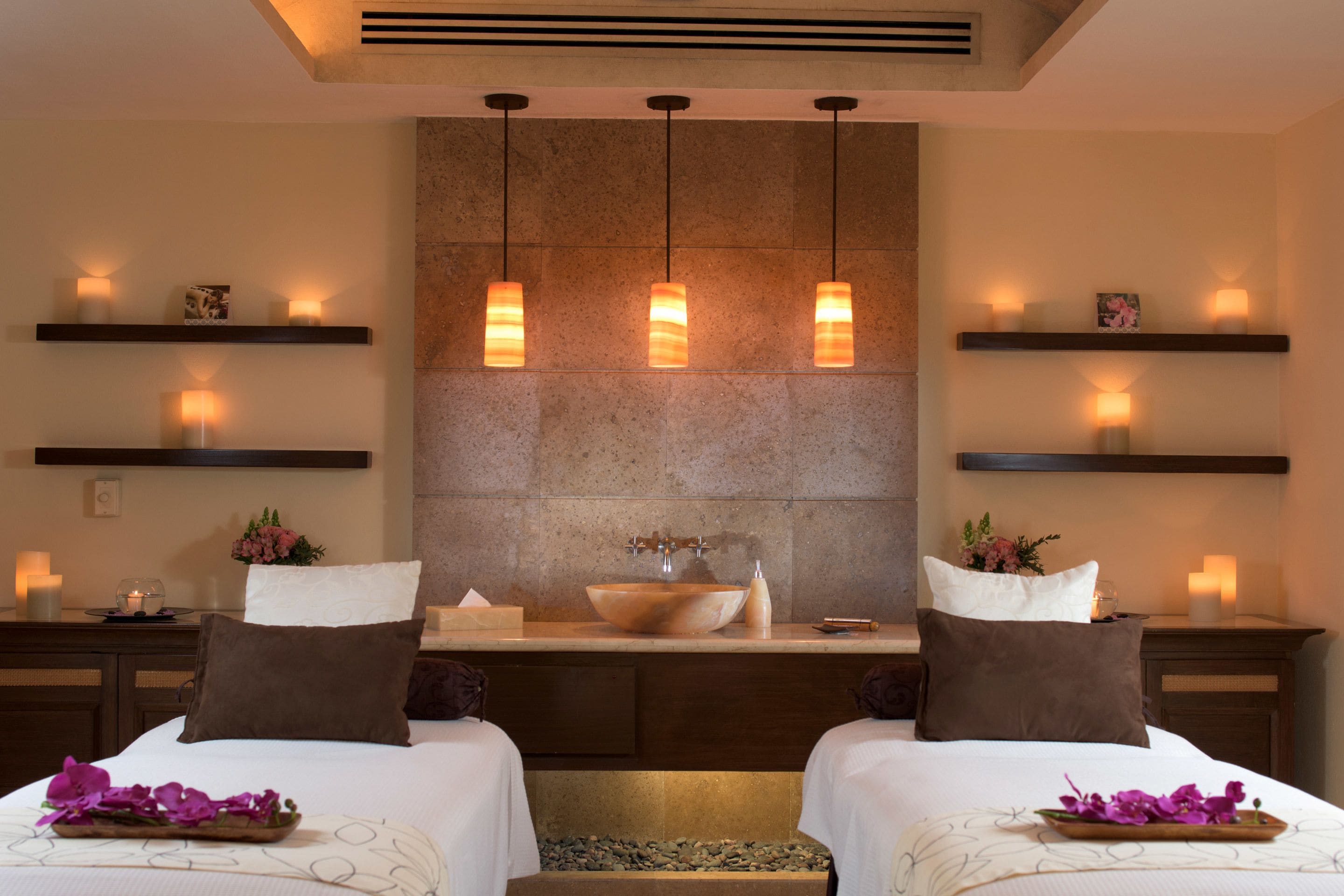 A hotel room with two beds, a large mirror, a sink, and pendant lights.