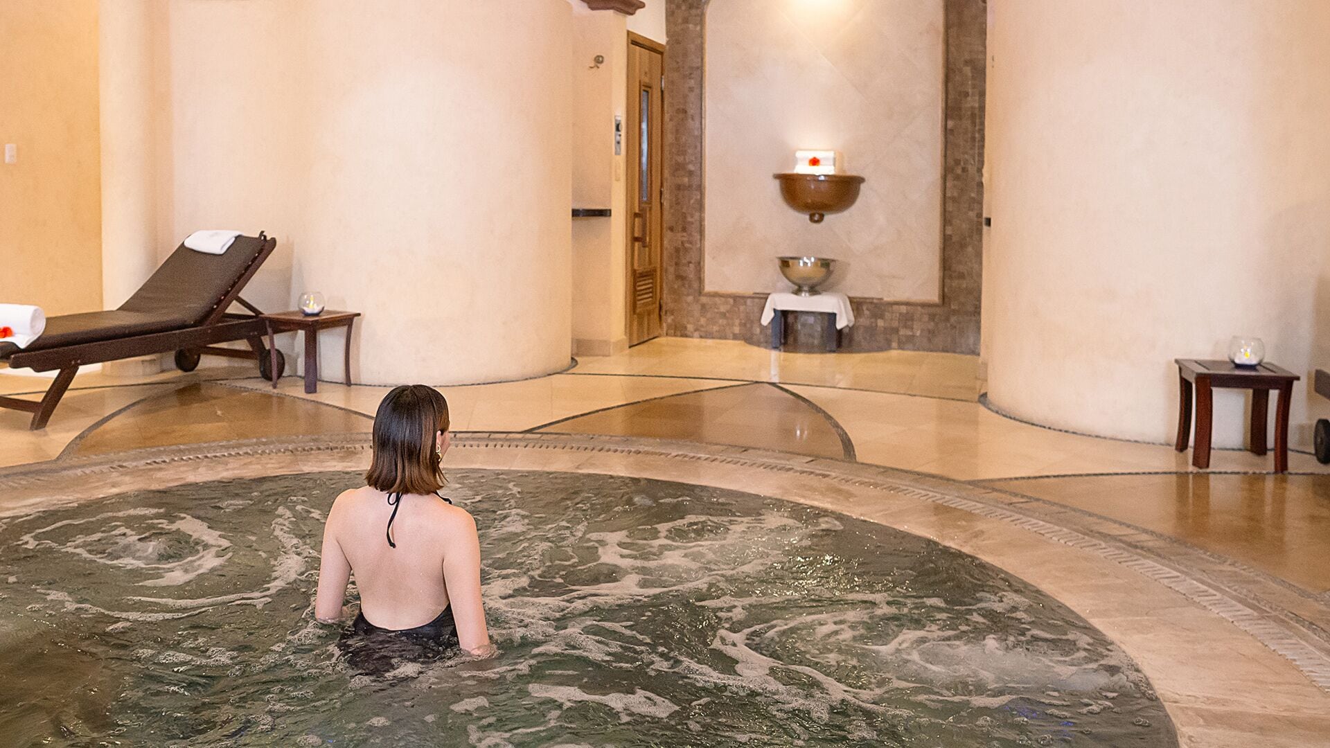 Eine Person in einem Thermalbad mit Liege und einem kleinen Tisch mit Kerze.