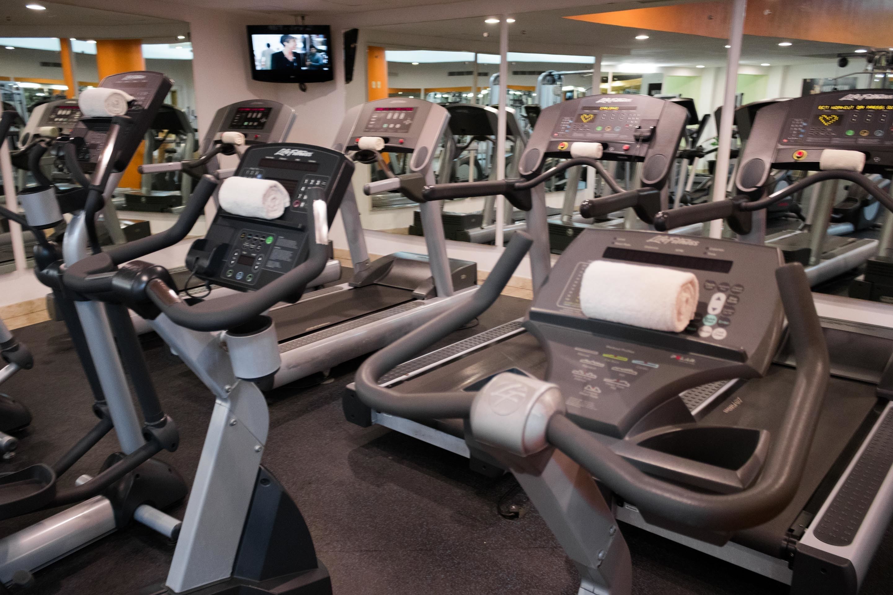 A row of stationary bikes in a gym with a TV mounted on the wall.