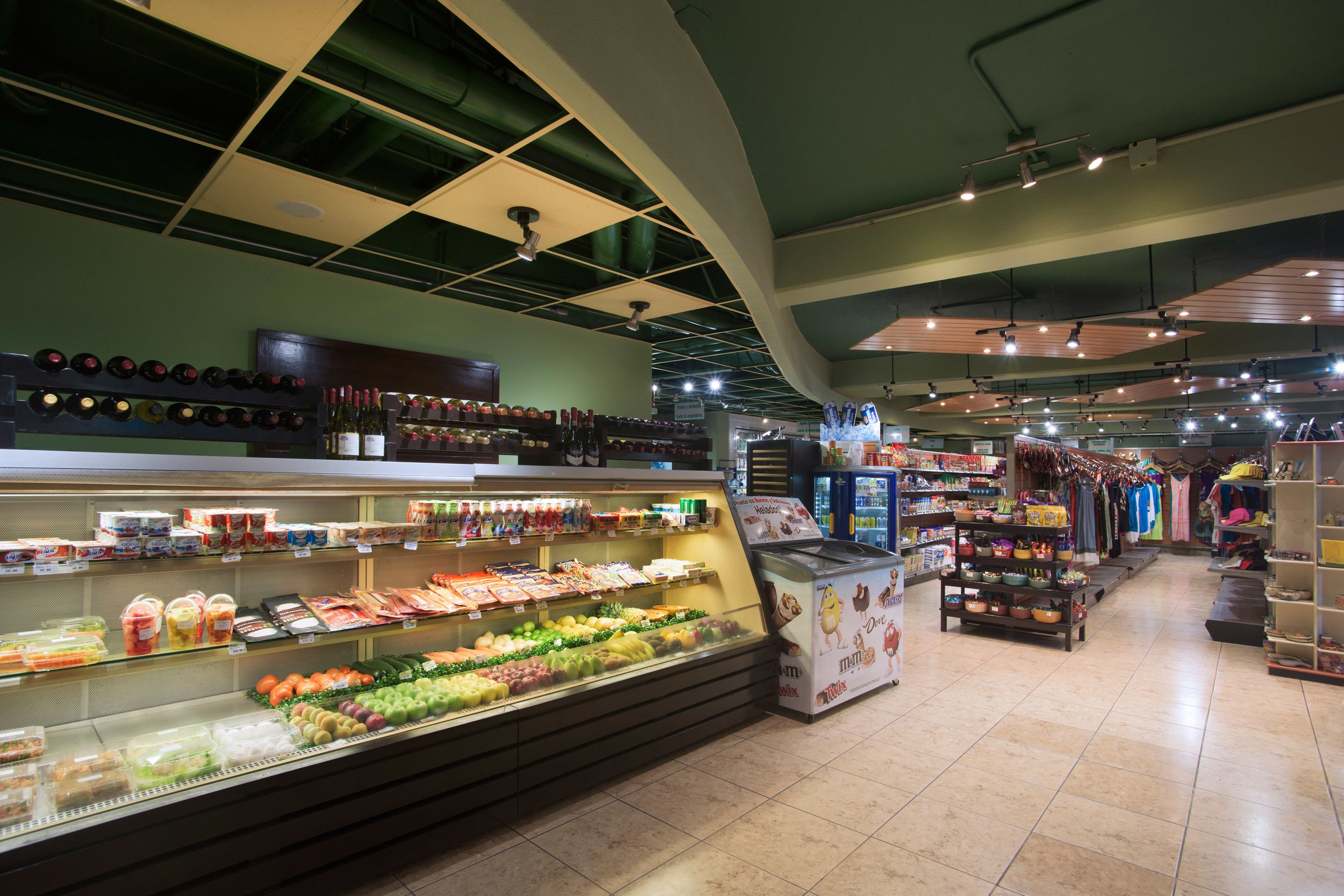 Interior de un supermercado con una barra de deli, sección refrigerada y diversos productos en los estantes.