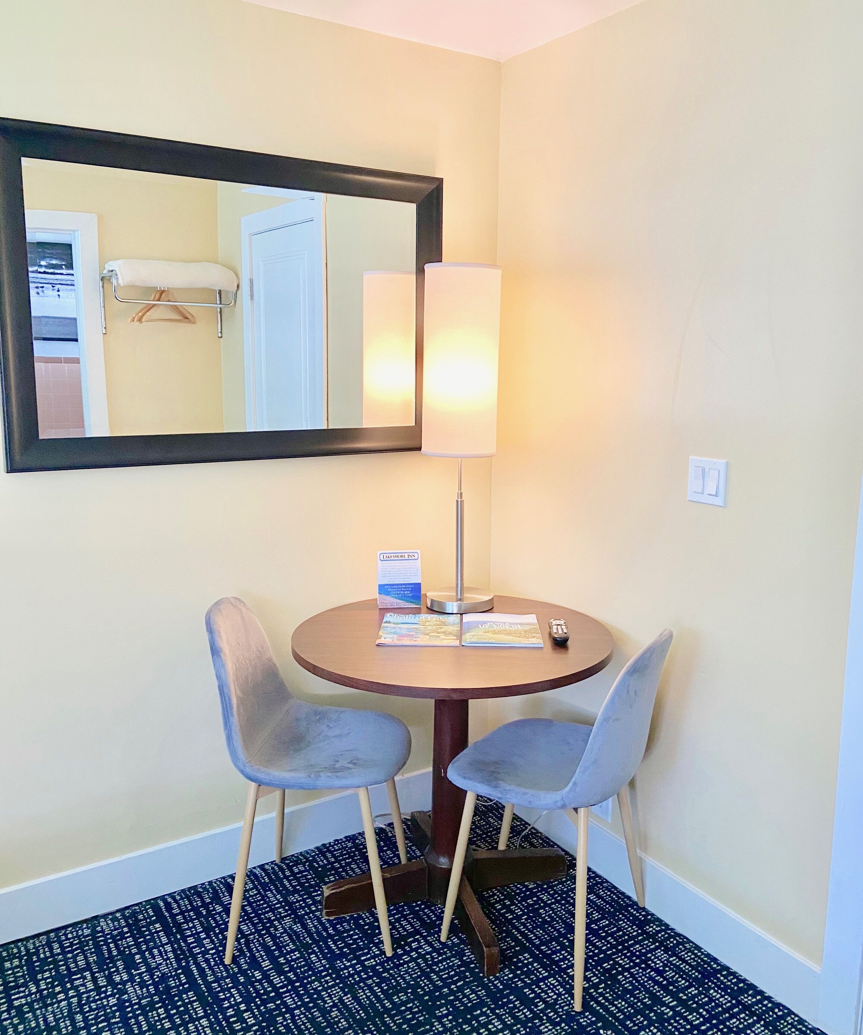 A hotel room with a round table, two chairs, a lamp, a mirror, and a sign indicating the room type.