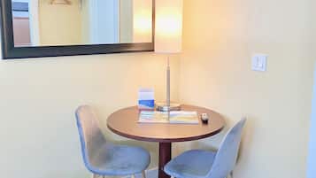 A hotel room with a round table, two chairs, a lamp, a mirror, and a sign indicating the room type.