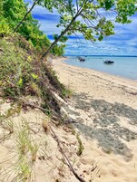 Una playa arenosa con barcos en el agua, vegetación en la orilla y un cielo despejado.