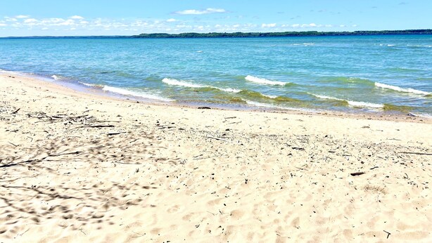 A beach with clear blue water and a sandy shore. - Elk Rapids Lakeshore Inn (Williamsburg)