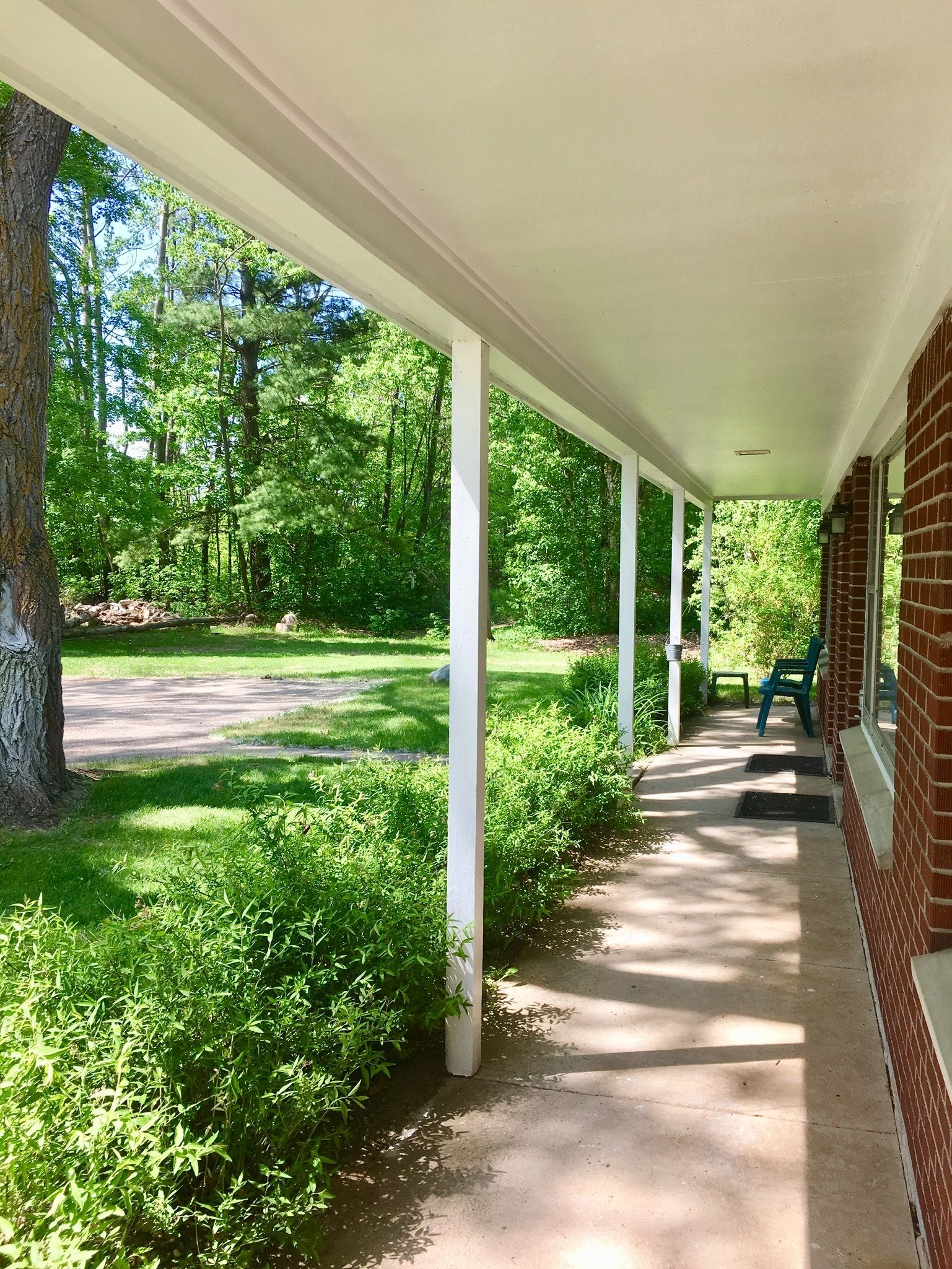A covered porch with white columns, a brick wall, and a view of a green, wooded area.