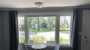 A hotel room with a large window, two chairs, a small table, and a bed. - Elk Rapids Lakeshore Inn (Williamsburg)