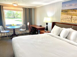 Habitación de hotel con una cama grande, un escritorio con silla, una mesita y una lámpara.